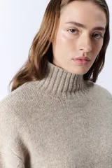 Polera de punto color beige, con cuello tortuga y diseño holgado.