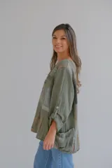 Blusa verde militar con estampado abstracto en tonos marrones, grises y negros. Tiene mangas 3/4 con botón y cuello redondo.