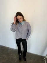 Camisa a rayas verticales azules y blancas, de popelina de algodón, con cuello verde y botones marmolados. Es corta adelante y larga atrás.
