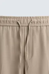 Pantalón color topo de corte recto, con cintura elástica ajustable con cordón, bolsillos laterales y bolsillos de vivo en la espalda.