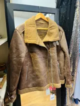 Campera marrón de gamulan con cuello y puños de piel sintética color beige, cierre lateral con cremallera y hebillas decorativas.