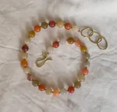 Gargantilla corta con cuentas redondas de piedra en tonos naranja, marrón, beige y blanco, unidas por pequeñas cuentas doradas.
