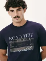 Camiseta blanca de algodón con cuello redondo y mangas cortas. Estampa rectangular con borde negro que contiene la frase "NATURAL ATMOSPHERE" en letras mayúsculas y una imagen de montañas y mar.