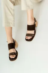 Sandalias de tacón de madera con tiras de gamuza marrón y detalles de tachas metálicas.