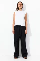 Pantalón negro de corte holgado en algodón, con tiro alto, cintura elástica fruncida y cordón para ajustar. Piernas anchas con bolsillos laterales.