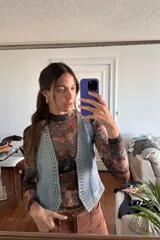 Chaleco negro de cuero con escote en V y cierre frontal con cordones. Presenta ojalillos metálicos plateados a lo largo de los bordes.