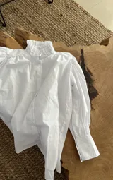 Camisa blanca de mangas largas abullonadas con puños fruncidos y cuello alto con volados.
