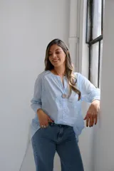 Blusa celeste de mangas largas con cuello redondo y abertura en V. Tiene detalles de bordado calado en el frente y un botón de madera.
