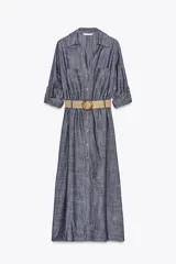 Vestido camisero azul con cinturón de rafia, de cuello solapa y manga tres cuartos con trabilla y botón. Tiene bolsillos de parche en el delantero y cierre frontal con botones.