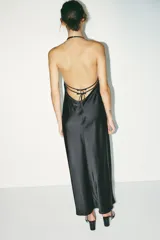 Vestido midi negro de satén con escote en V y tirantes finos. Detalle de tiras cruzadas en la espalda con lazadas. Cierre trasero con cremallera.
