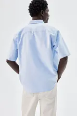 Camisa celeste de algodón Oxford con cuello abotonado, manga corta, bolsillo de parche en el pecho y corte regular.