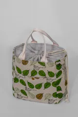 Lunchera térmica de tela color beige con estampado de hojas verdes y marrones. Tiene doble asa de tela color crudo y cierre con cordón ajustable.