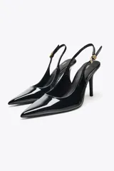 Zapato de tacón destalonado color negro charol, con punta fina y tira trasera con hebilla metálica dorada.