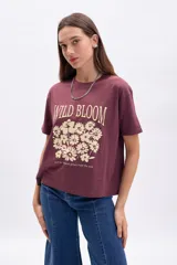 Remera color borgoña de corte recto y mangas cortas, con estampa frontal de flores y texto en color crema.