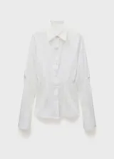 Camisa blanca de algodón con cuello camisero, corte recto, mangas largas con pliegues y puños abotonados.