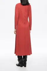 Vestido de largo midi en color negro con corte en línea A y vuelo. Posee escote barco, mangas largas tipo murciélago ajustadas en los puños y detalles de pespuntes decorativos a contraste. Está confeccionado en una mezcla de cupro y elastano.