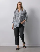 Camisa de mujer estampada con hojas en blanco y negro, cuello con solapa, abertura central con botones, bolsillos aplicados en el delantero y mangas largas con lazo.