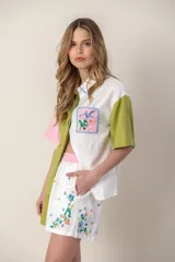 Camisa de mangas cortas con diseño color block en verde, blanco y rosa. Tiene un bolsillo con bordado de ave y flores bordadas en el frente.