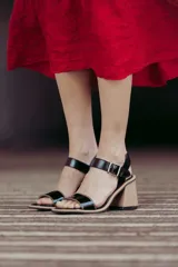 Sandalias de cuero charol negro con tira delantera y tobillera con hebilla metálica. Taco de madera con forma geométrica.