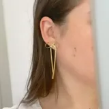 Par de aros colgantes dorados con forma de moño, confeccionados en acero quirúrgico hipoalergénico con baño de oro de 18K.