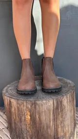 Botas Chelsea de cuero color marrón, con elástico lateral, suela negra gruesa y pespuntes blancos.