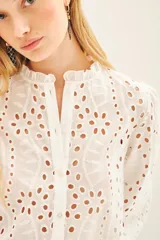 Camisa celeste de broderie de algodón con calado de hojas. Tiene cuello redondo con volados, mangas largas abullonadas con puños elásticos y cierre frontal con botones.