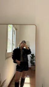 Campera corta negra de ecocuero con cuello camisero, cierre frontal con botones a presión, dos bolsillos con solapa y mangas largas con puños abotonados.