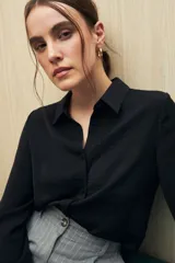 Camisa blanca de manga larga con textura sutil y caída fluida. Presenta cuello clásico, botones forrados a tono y puños con terminación fruncida.