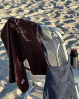 Remera marrón de corte oversize confeccionada en jersey de algodón, con estampa en la espalda con el texto "The Tribu Brand Creative Studio" en color crema y un diseño de tres líneas horizontales debajo.