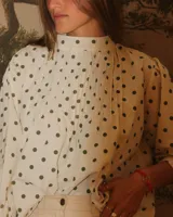 Camisa color crema con estampado de lunares verdes, cuello alto y mangas largas abullonadas.