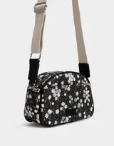 Bandolera negra con estampado de flores blancas, correa de algodón ajustable y cierre superior.