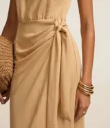 Vestido midi color beige, corte evasé, sin mangas, con lazo lateral y cierre trasero con cremallera.
