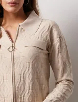 Cardigan color beige en tejido jacquard, con cuello con solapa y abertura central con cierre. Delantera con bolsillos simulados.