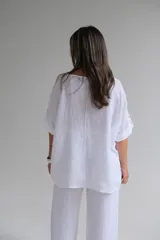 Blusa blanca de lino con cuello redondo y mangas 3/4 con botón. Tiene un bolsillo en el pecho y apliques estampados con motivos florales.