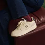 Championes urbanos Lacoste modelo L001 Set 224 2 SMA, color blanco hueso con detalles en azul marino y rojo. Presentan el logo de la marca bordado en el lateral y suela de goma color caramelo.
