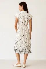 Vestido camisero midi negro con lunares blancos, de manga corta, cuello camisero, cierre frontal con botones y bolsillos laterales.