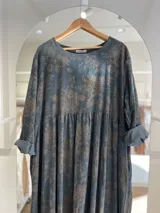 Vestido largo de pana fina color gris azulado con estampado floral en tonos beige. Diseño oversize con mangas largas y puños arremangados.