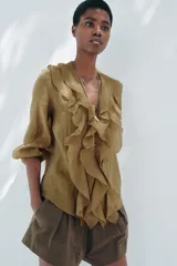 Camisa color verde oliva de tela traslúcida con escote en V, mangas largas abullonadas con puños elásticos y volantes en el frente.