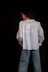 Camisa color crema con cuello alto y mangas largas con volados en los puños. Presenta detalles de crochet y broderie en el frente.