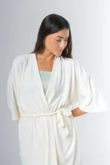 Bata tipo kimono de algodón color blanco hueso, con textura acanalada vertical. Presenta un cruce frontal asegurado con un lazo a la cintura y mangas anchas de largo al codo.