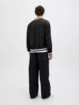 Campera bomber negra con cuello tipo baseball y puños de canalé. Cierre frontal con botones a presión y bolsillos laterales.