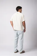 Camisa de manga corta color crudo, confeccionada en lino texturizado. Tiene cuello tipo cubano, cierre frontal con botones y corte recto.