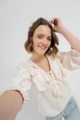 Blusa color crema con volados en el frente, detalle de puntilla y bordados florales en mangas.