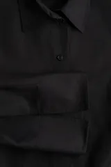 Camisa negra oversized de algodón con cuello clásico, abotonadura frontal, mangas largas con hombros caídos, puños con abertura y bajo recto.