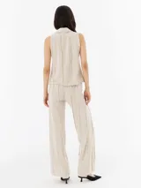 Pantalón de lino color beige, de corte recto y tiro alto, con detalle de flecos verticales.