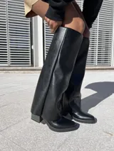 Botas negras de ecocuero, estilo texanas, de caña alta y taco cuadrado.