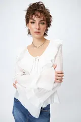 Blusa blanca de gasa con escote en V y volados en el cuello y las mangas largas. Se ata con lazos finos al frente.