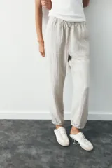 Pantalón jogger color gris claro, de tiro alto con cintura elástica ajustable con cordones, bolsillos delanteros y traseros con solapa, y puños elásticos en el bajo.