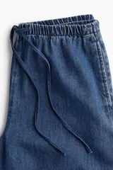 Pantalón de denim azul de corte holgado, con cintura elástica ajustable con cordón, bolsillos laterales y piernas anchas.
