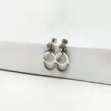 Par de aros colgantes plateados, tipo pendulares. Cada aro consta de tres secciones: un poste superior con circonias, un anillo liso intermedio y una pieza inferior en forma de herradura con circonias engastadas.